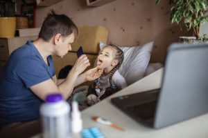 father checking his daughters throat during telehealth visit