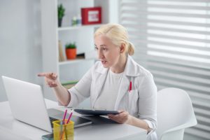 severe looking caucasian female doctor pointing at laptop for telehealth visit